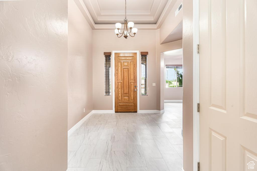 Entrance foyer with a chandelier, baseboards, ornamental molding, light marble finish floors, and a tray ceiling