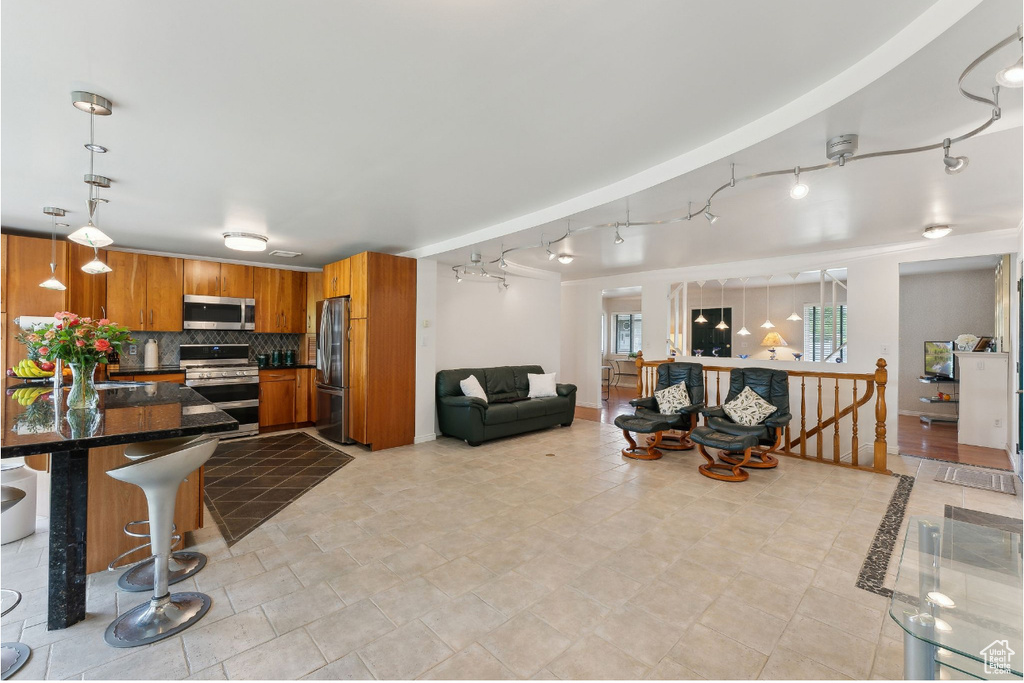 Kitchen with stainless steel appliances, track lighting, brown cabinets, a kitchen bar, and open floor plan