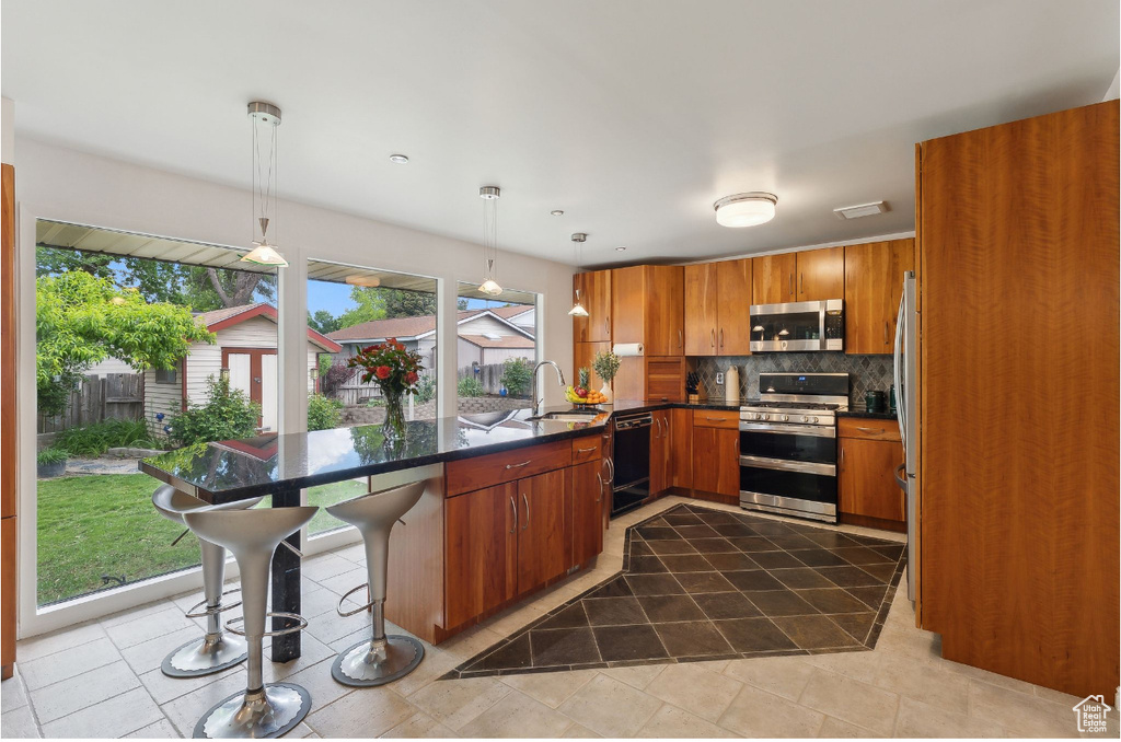Kitchen featuring appliances with stainless steel finishes, backsplash, a peninsula, brown cabinets, and dark countertops