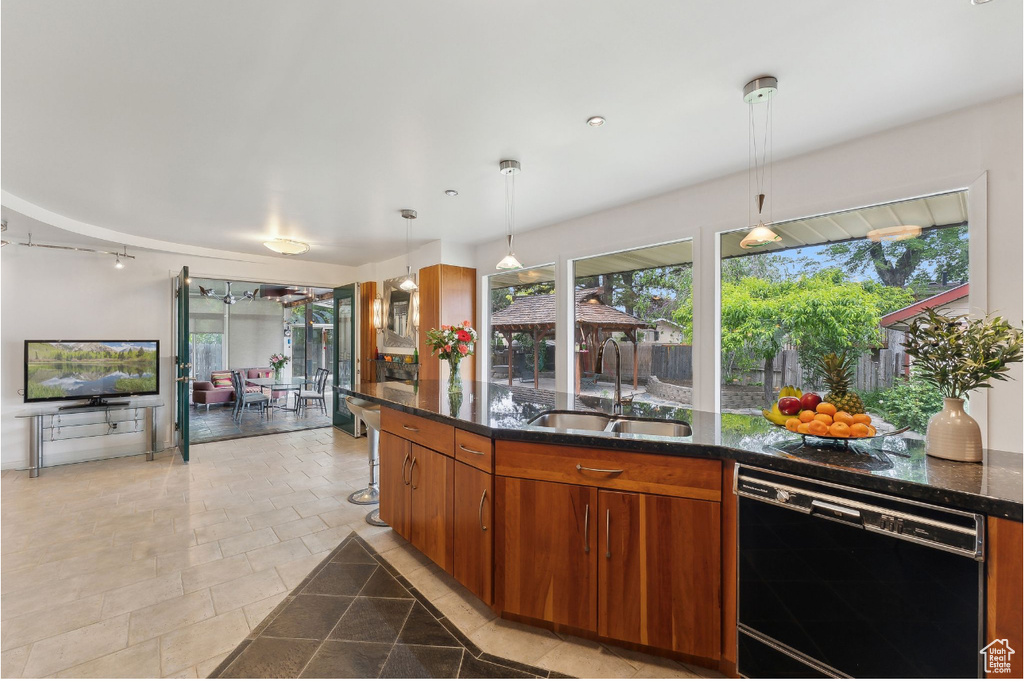 Kitchen with dishwasher, a sink, brown cabinets, hanging light fixtures, and dark stone countertops