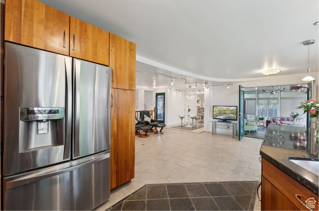 Kitchen with stainless steel fridge with ice dispenser, brown cabinetry, rail lighting, open floor plan, and tile patterned flooring