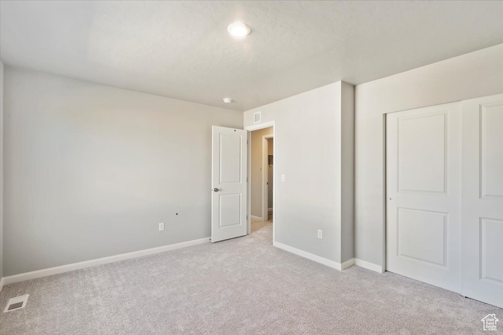 Unfurnished bedroom with light carpet, baseboards, and a closet