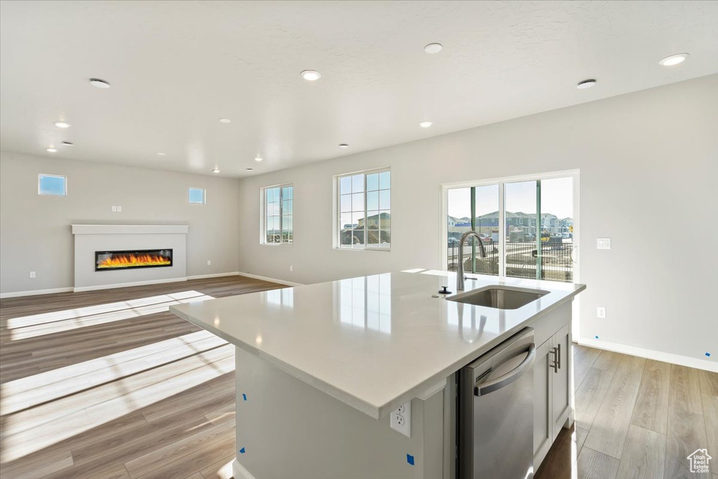 Kitchen with dishwasher, a sink, light wood-style floors, a glass covered fireplace, and recessed lighting