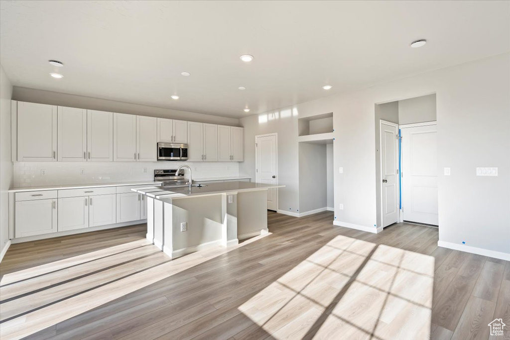 Kitchen featuring appliances with stainless steel finishes, a center island with sink, baseboards, light countertops, and recessed lighting
