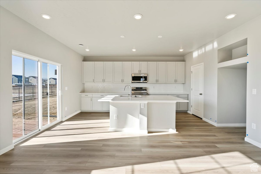 Kitchen with appliances with stainless steel finishes, light countertops, an island with sink, light wood-style flooring, and recessed lighting