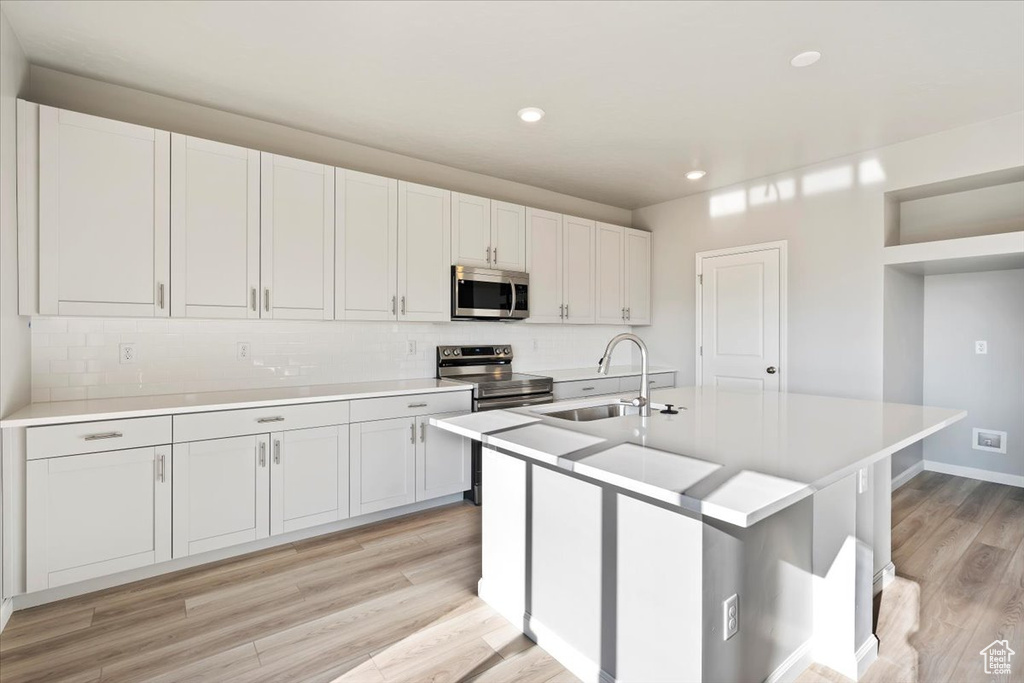 Kitchen with appliances with stainless steel finishes, a sink, light wood-type flooring, light countertops, and backsplash