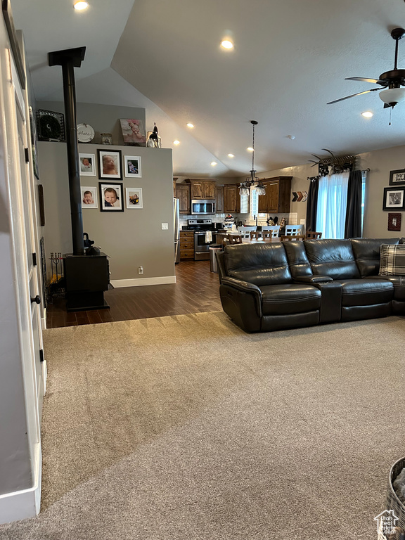 Carpeted living room featuring ceiling fan, vaulted ceiling, and a wood stove