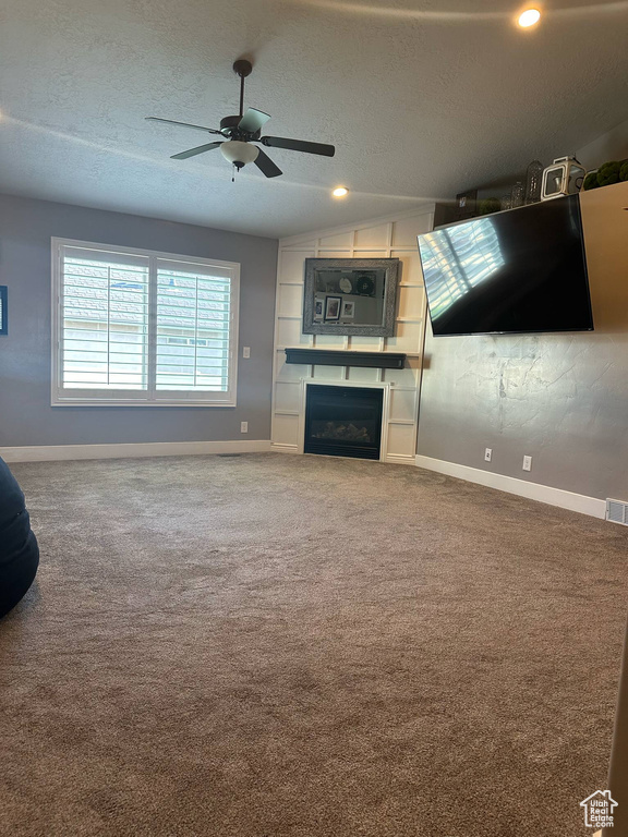 Unfurnished living room with baseboards, carpet, a textured ceiling, a ceiling fan, and a fireplace