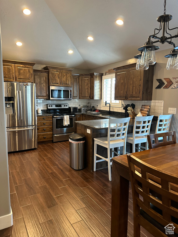 Kitchen featuring a chandelier, tasteful backsplash, dark wood-type flooring, appliances with stainless steel finishes, and pendant lighting