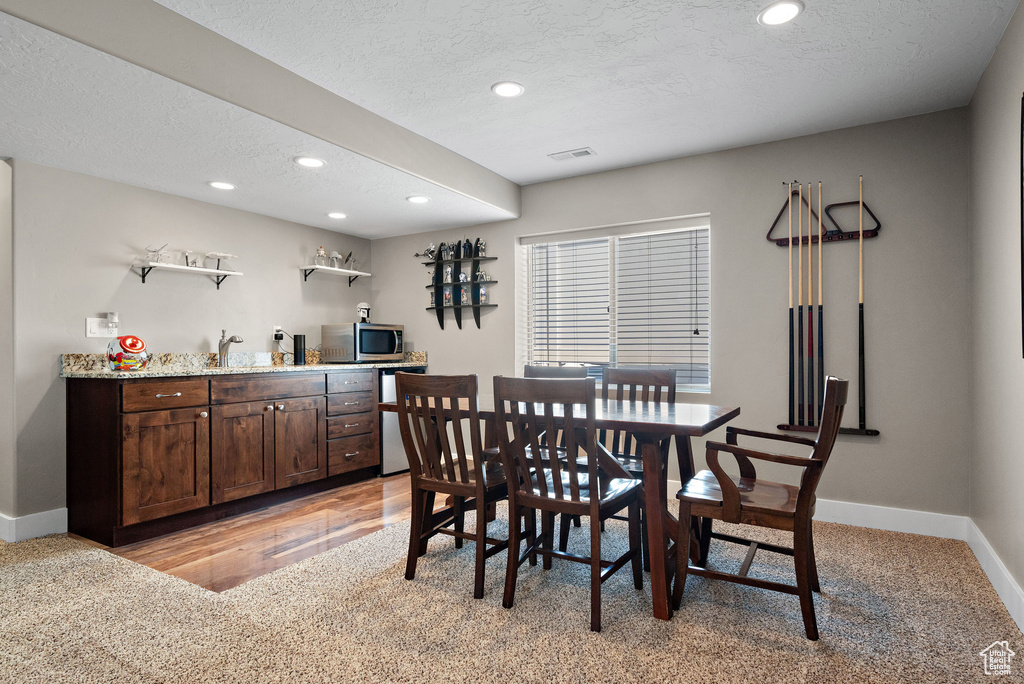 Dining space with bar with sink, recessed lighting, baseboards, light colored carpet, and a textured ceiling