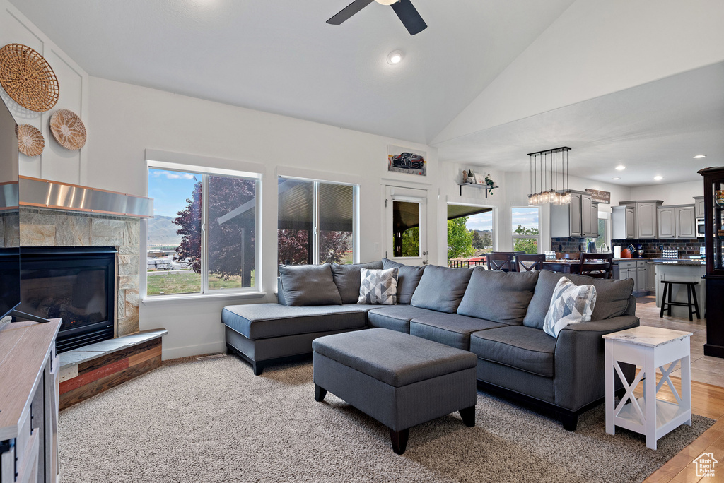 Living area featuring plenty of natural light, ceiling fan, a glass covered fireplace, lofted ceiling, and light wood finished floors