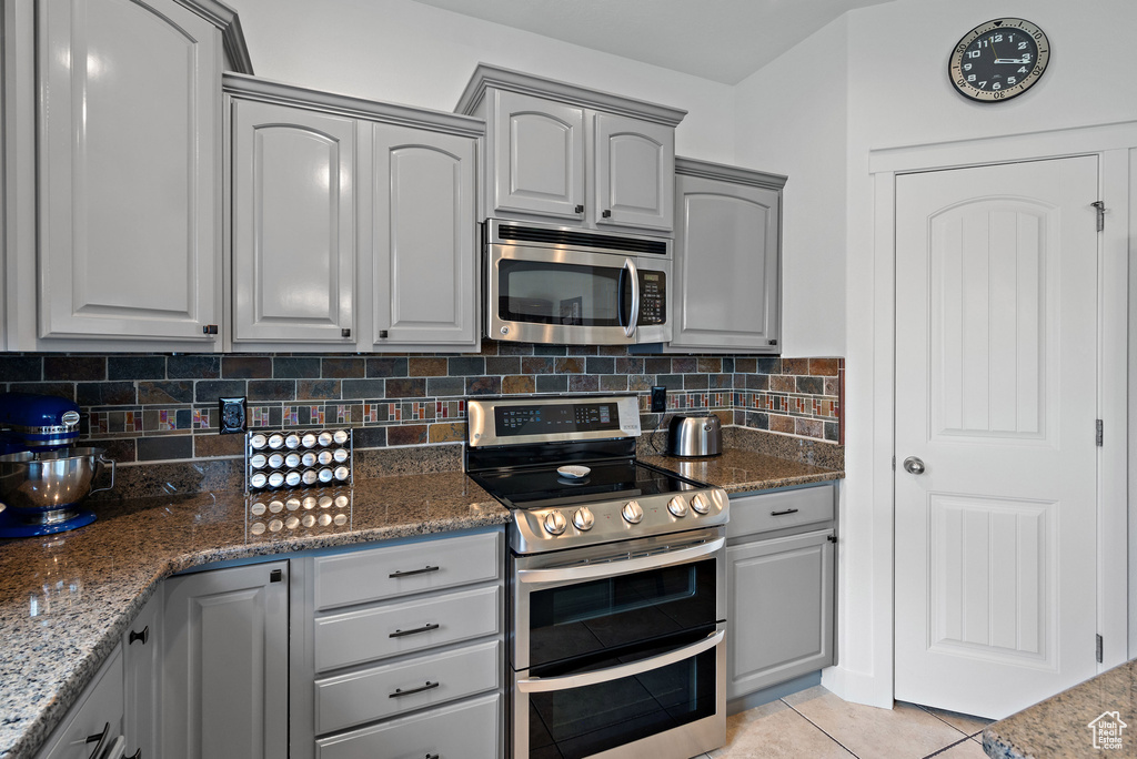 Kitchen featuring stainless steel appliances, gray cabinetry, light tile patterned floors, and tasteful backsplash