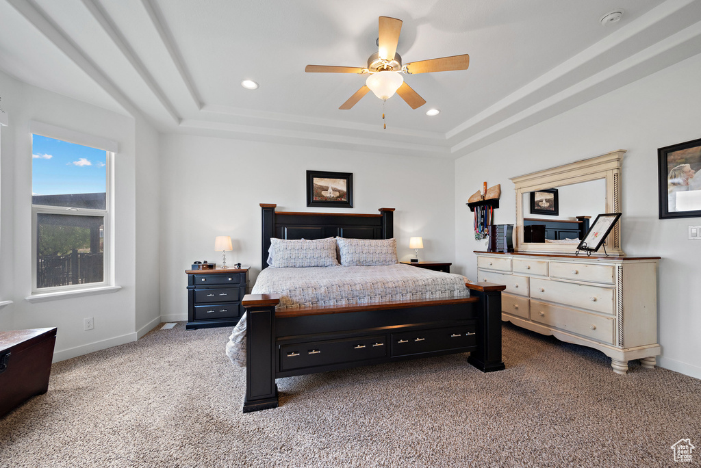 Bedroom with light colored carpet, a raised ceiling, baseboards, recessed lighting, and ceiling fan