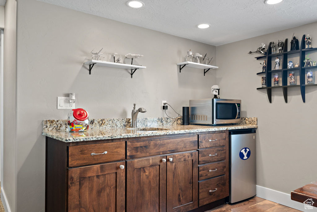 Indoor wet bar with stainless steel microwave, refrigerator, baseboards, light wood finished floors, and recessed lighting