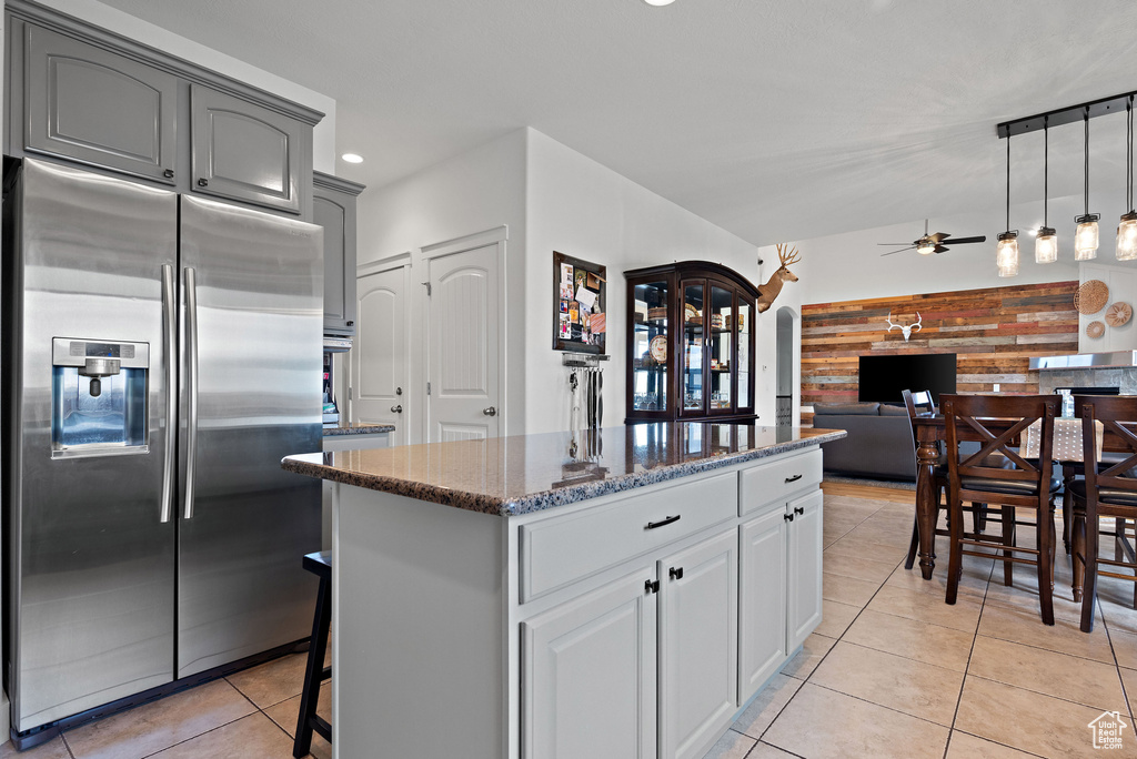 Kitchen featuring stainless steel refrigerator with ice dispenser, light tile patterned floors, dark stone counters, a kitchen island, and a ceiling fan