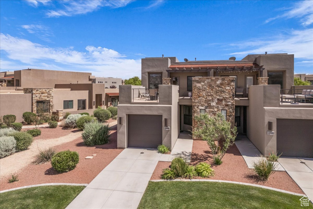Southwest-style home with a balcony, stone siding, stucco siding, and concrete driveway