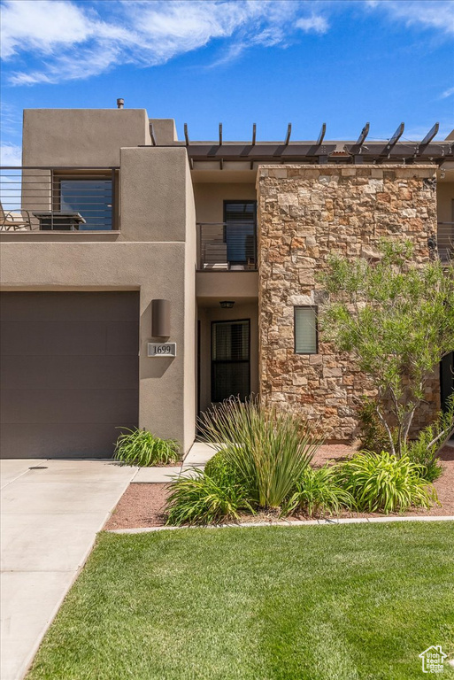 View of front of house featuring a balcony, stone siding, stucco siding, driveway, and a front lawn