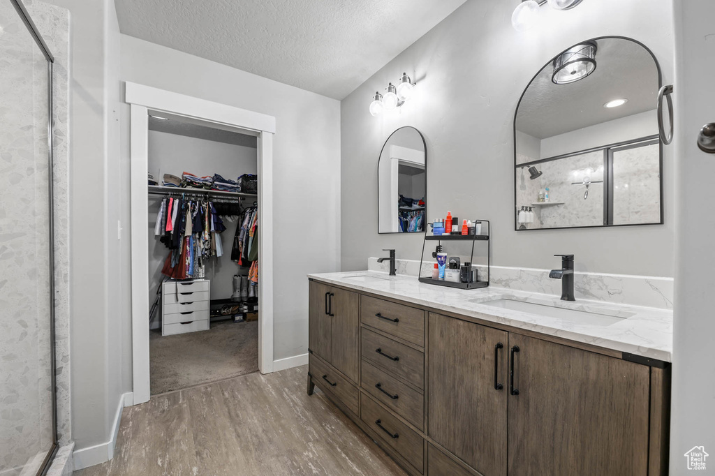 Full bath featuring wood finished floors, a shower stall, a spacious closet, double vanity, and a textured ceiling