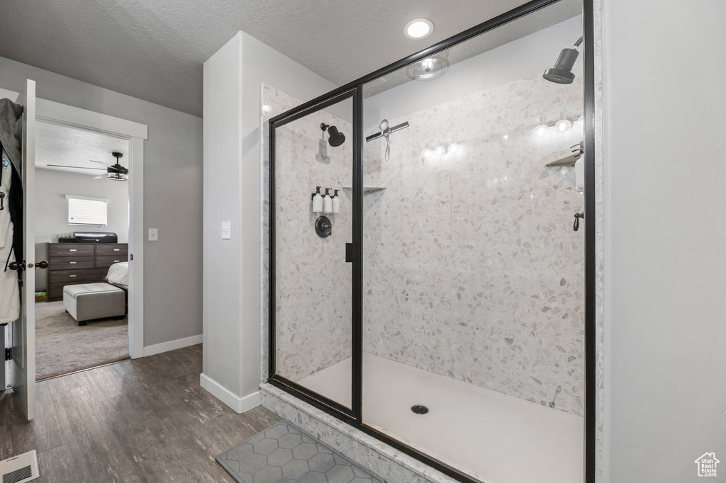 Ensuite bathroom featuring wood finished floors, a stall shower, baseboards, ceiling fan, and a textured ceiling