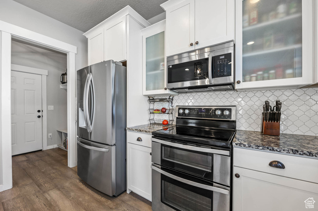 Kitchen featuring stainless steel appliances, white cabinetry, dark stone countertops, decorative backsplash, and a textured ceiling