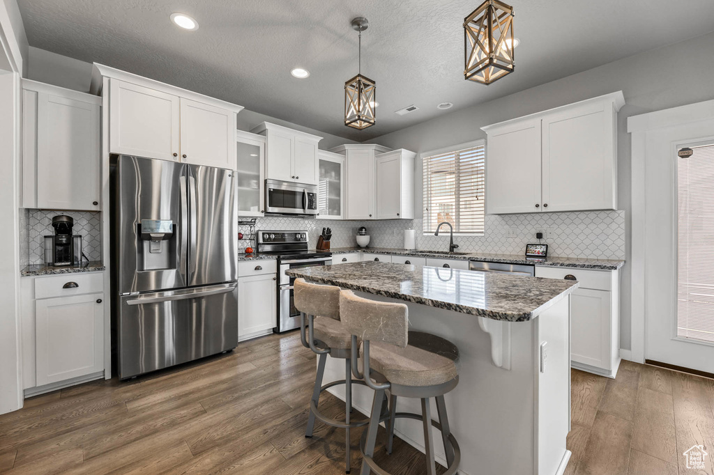 Kitchen featuring stainless steel appliances, recessed lighting, white cabinetry, dark wood-style floors, and a breakfast bar