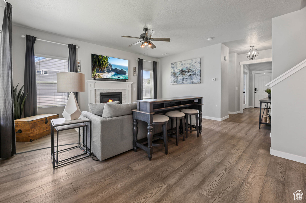 Living area featuring ceiling fan, wood finished floors, a glass covered fireplace, baseboards, and a textured ceiling
