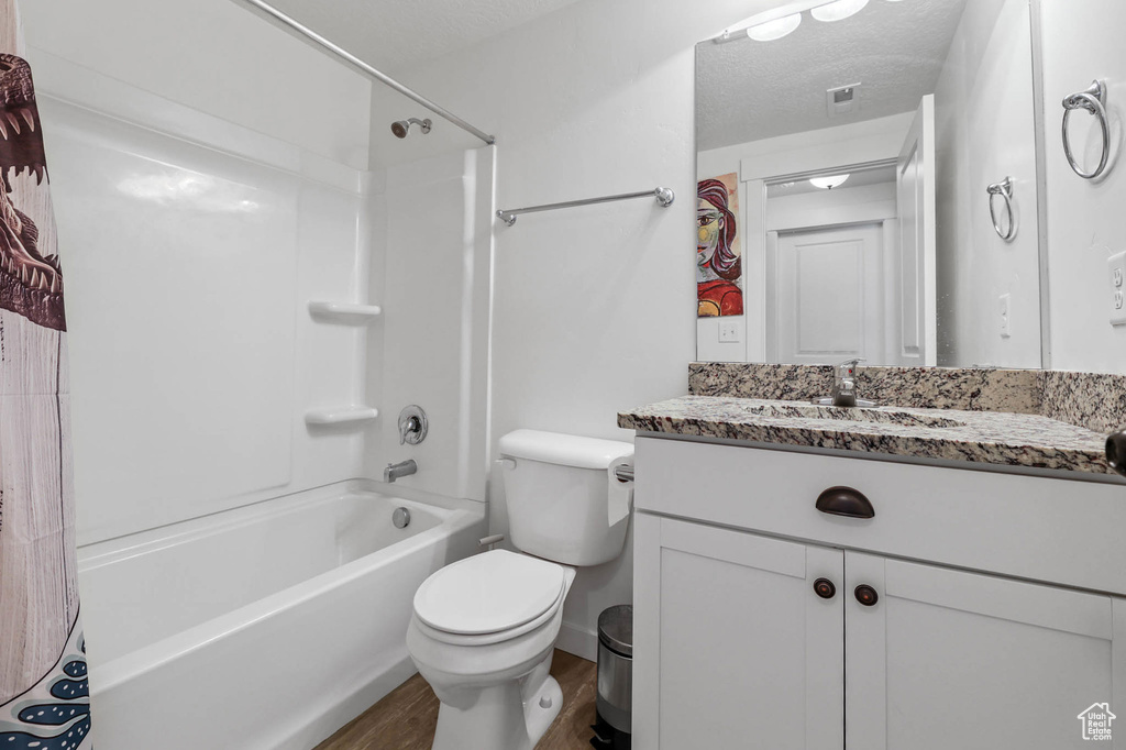 Full bath featuring vanity, wood finished floors, toilet, shower / tub combo with curtain, and a textured ceiling