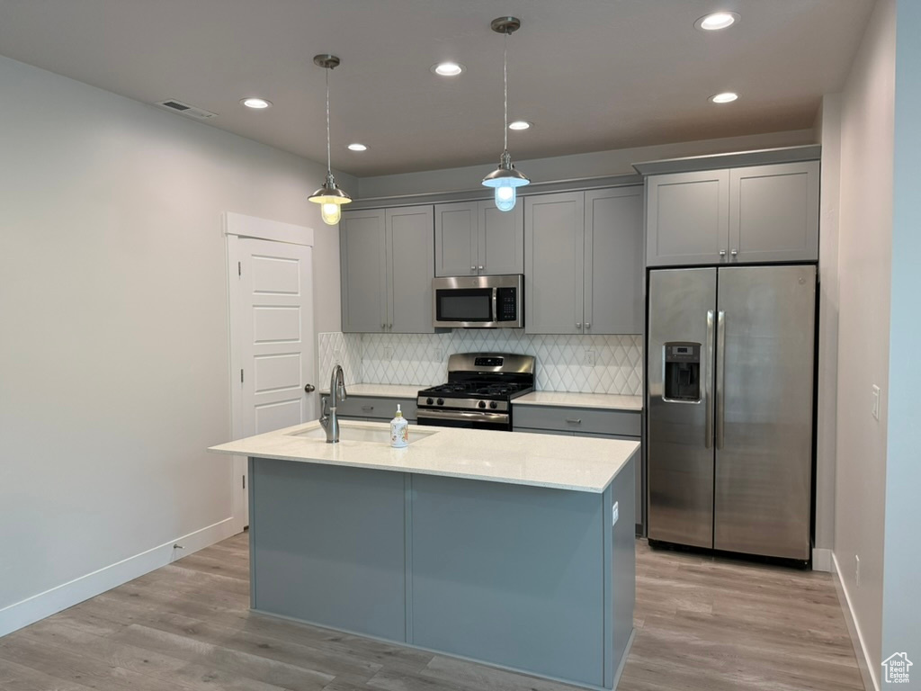 Kitchen featuring stainless steel appliances, a sink, gray cabinetry, an island with sink, and recessed lighting