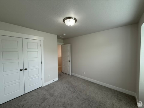 Unfurnished bedroom with carpet, baseboards, a closet, and a textured ceiling
