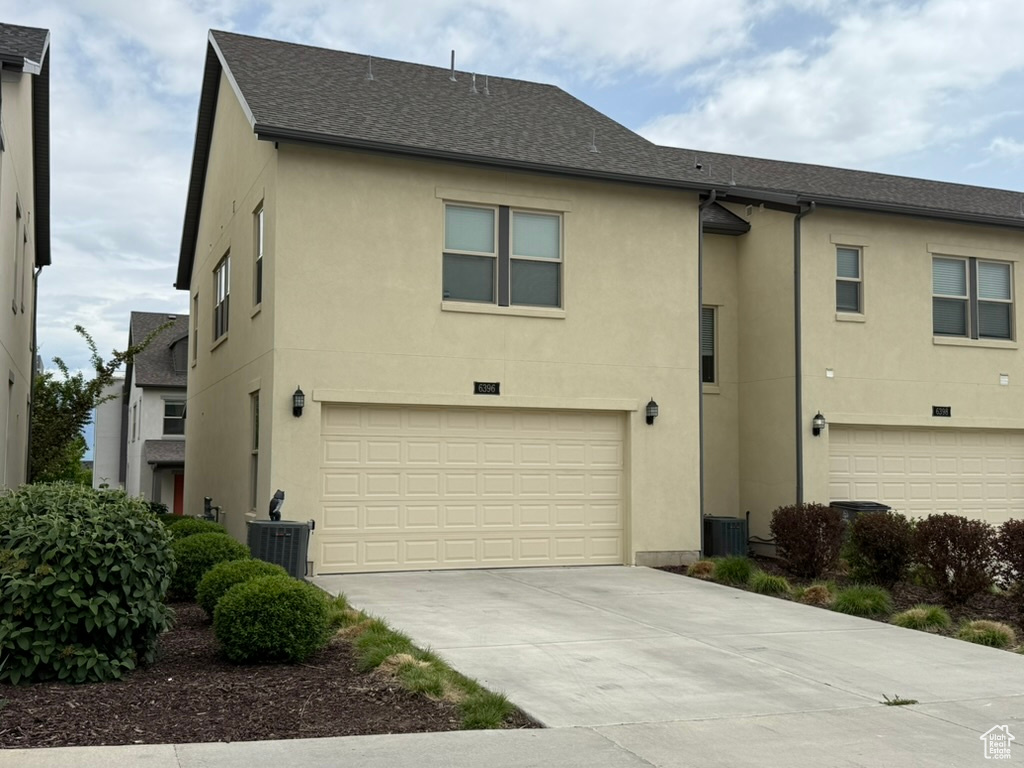 View of front of home with stucco siding, a garage, concrete driveway, and roof with shingles