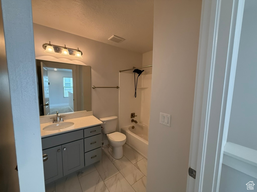 Bathroom with marble finish floors, toilet, vanity, shower / bathtub combination, and a textured ceiling