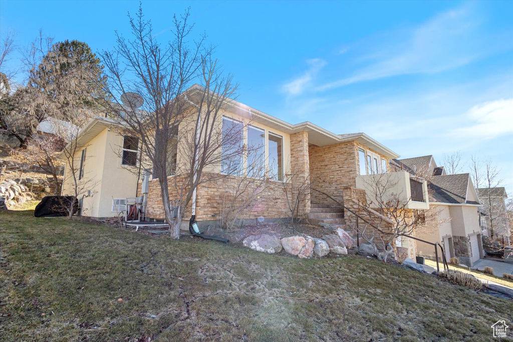 View of property exterior with stucco siding, a lawn, and stone siding