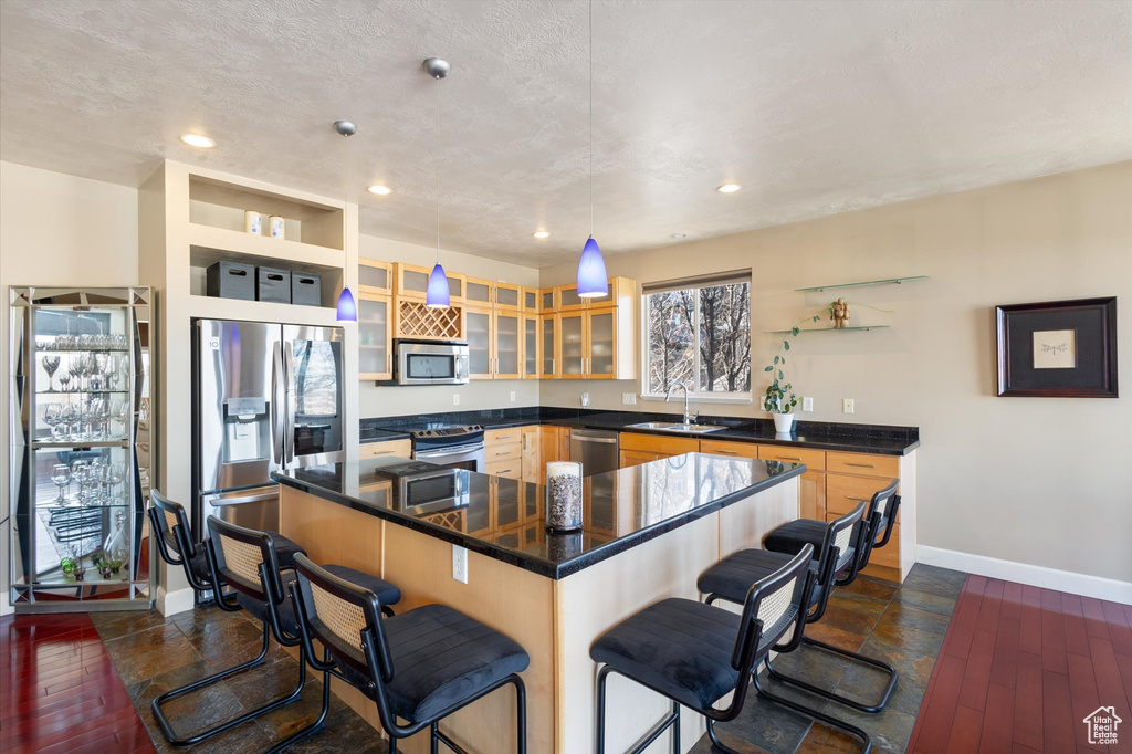 Kitchen featuring appliances with stainless steel finishes, a sink, baseboards, a kitchen breakfast bar, and dark countertops