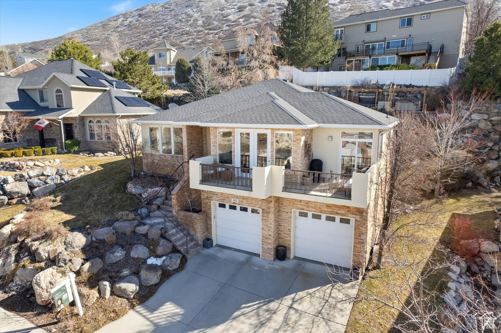 View of front of house with driveway, a garage, a mountain view, a balcony, and a shingled roof