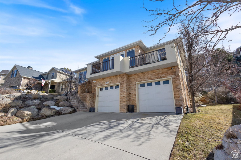 View of front of home with concrete driveway, a balcony, a garage, stairs, and stone siding