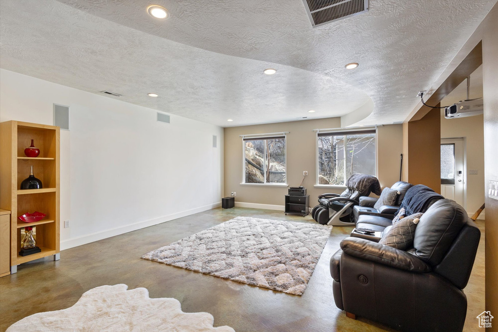 Living room featuring a textured ceiling, concrete flooring, baseboards, and recessed lighting