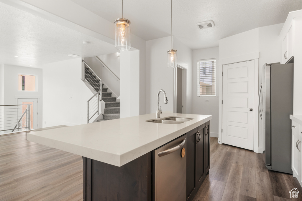 Kitchen featuring a sink, stainless steel appliances, light countertops, wood finished floors, and an island with sink