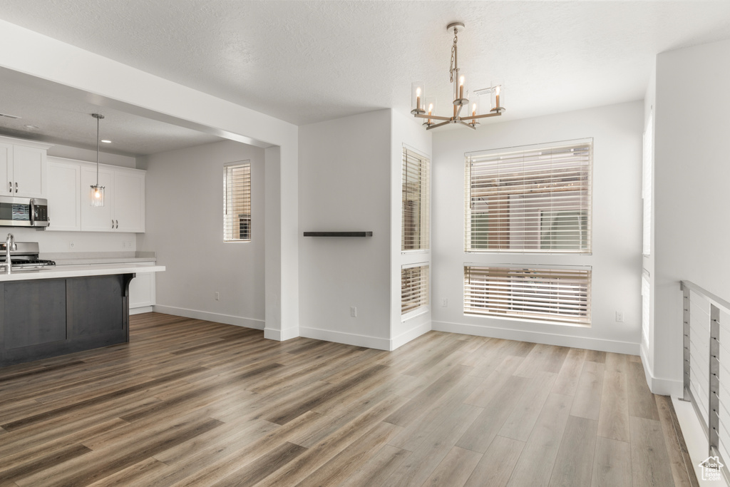 Kitchen featuring appliances with stainless steel finishes, light countertops, a chandelier, light wood-style floors, and white cabinets