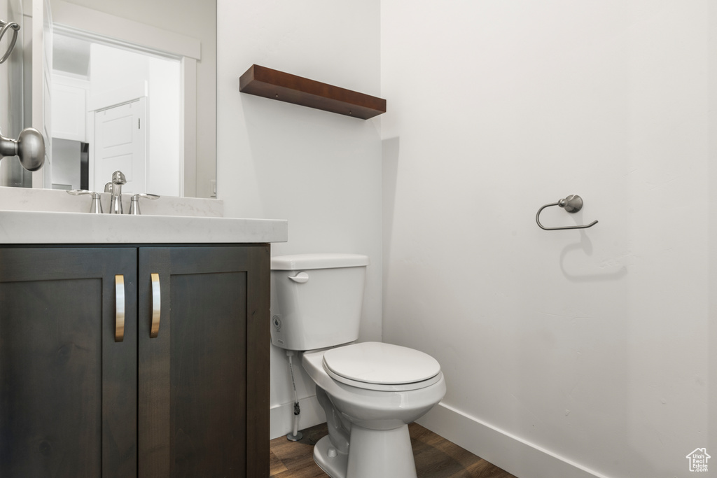 Half bath with wood finished floors, toilet, vanity, and baseboards