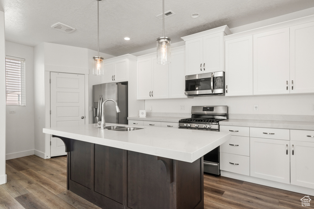 Kitchen with stainless steel appliances, a sink, a kitchen island with sink, white cabinets, and recessed lighting