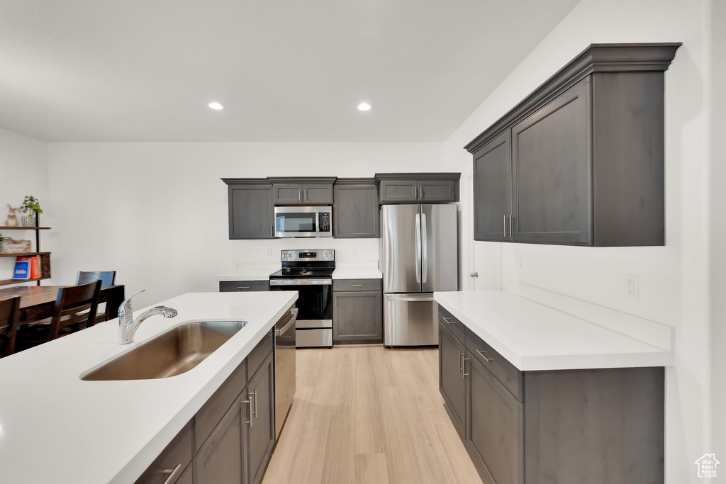 Kitchen with appliances with stainless steel finishes, a sink, light wood-type flooring, light countertops, and recessed lighting