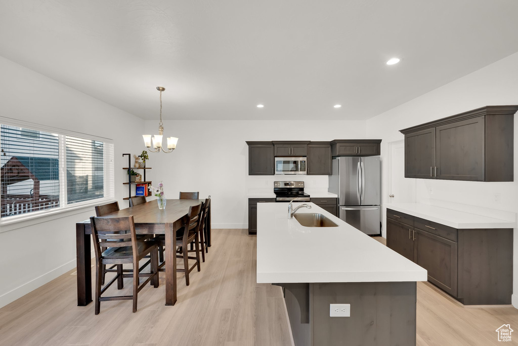 Kitchen with appliances with stainless steel finishes, a sink, light wood-type flooring, baseboards, and a chandelier