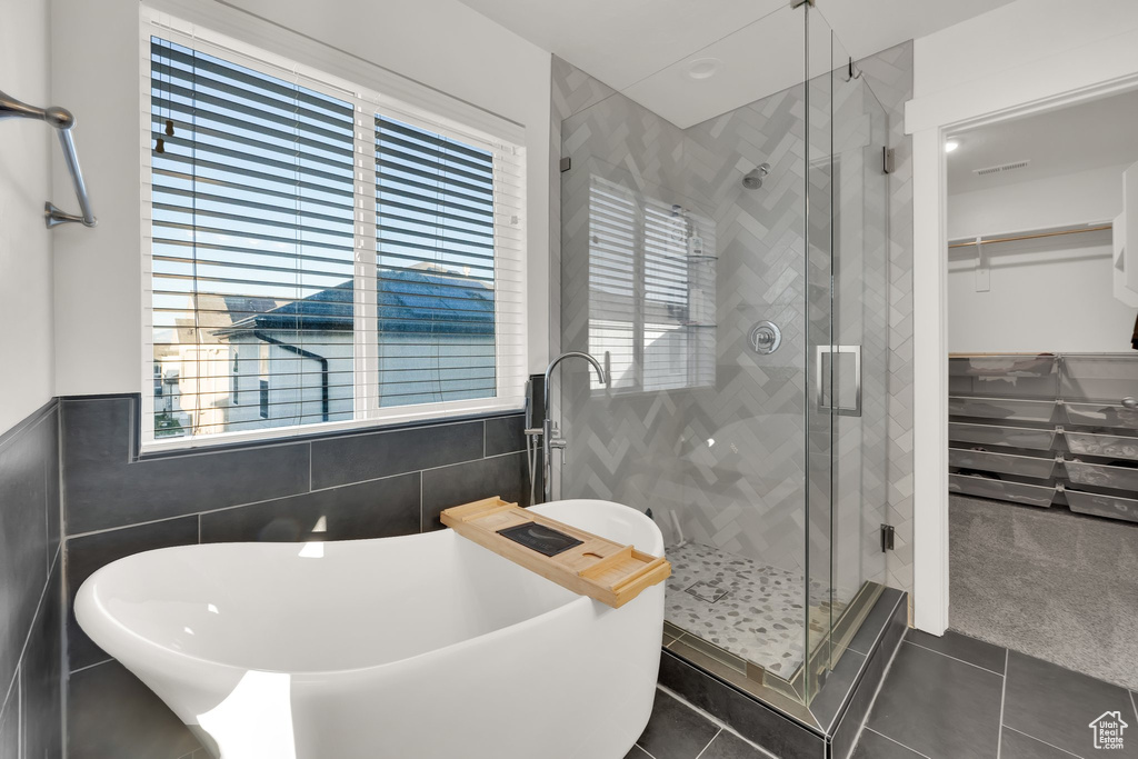 Full bathroom with tile walls, a stall shower, tile patterned floors, a freestanding tub, and a walk in closet