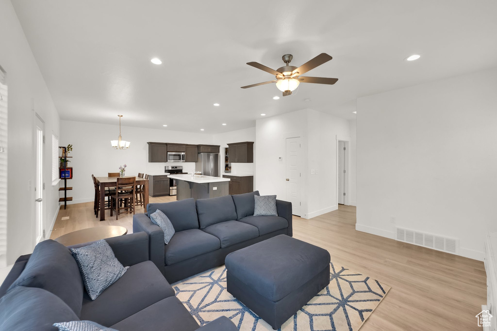 Living room featuring light wood-style flooring, a ceiling fan, baseboards, recessed lighting, and a chandelier