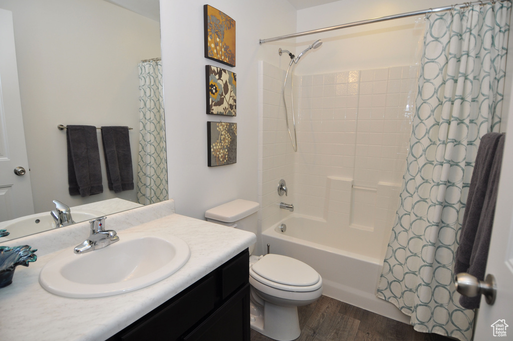 Bathroom with toilet, wood finished floors, vanity, and shower / bath combination with curtain