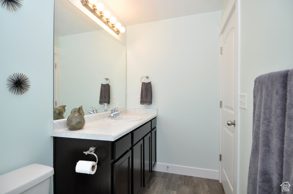 Half bathroom with wood finished floors, toilet, vanity, and baseboards