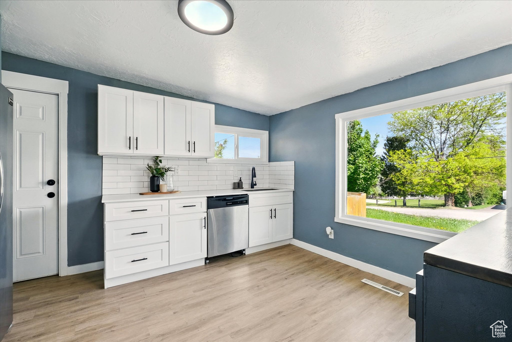 Kitchen featuring stainless steel dishwasher, baseboards, decorative backsplash, a sink, and white cabinets