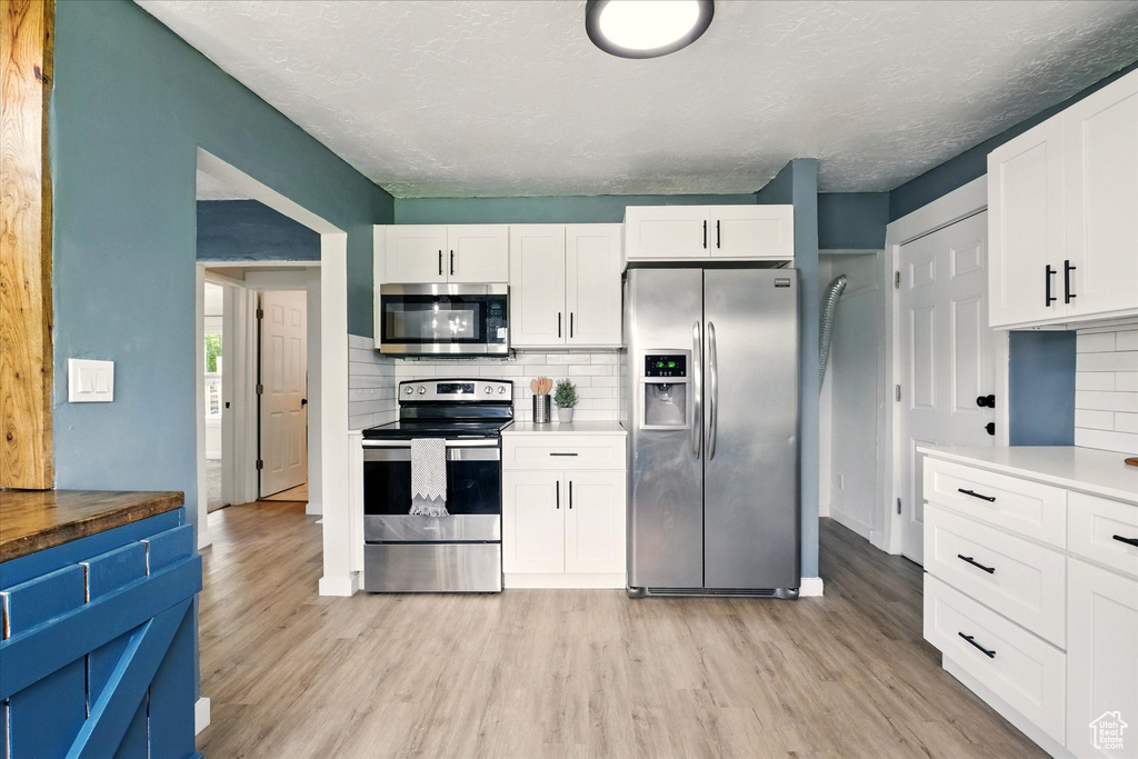 Kitchen with appliances with stainless steel finishes, light wood finished floors, decorative backsplash, white cabinets, and a textured ceiling