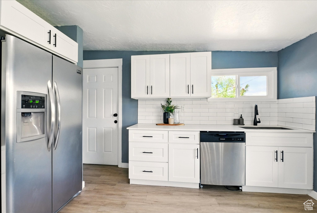 Kitchen featuring appliances with stainless steel finishes, a sink, tasteful backsplash, and white cabinets