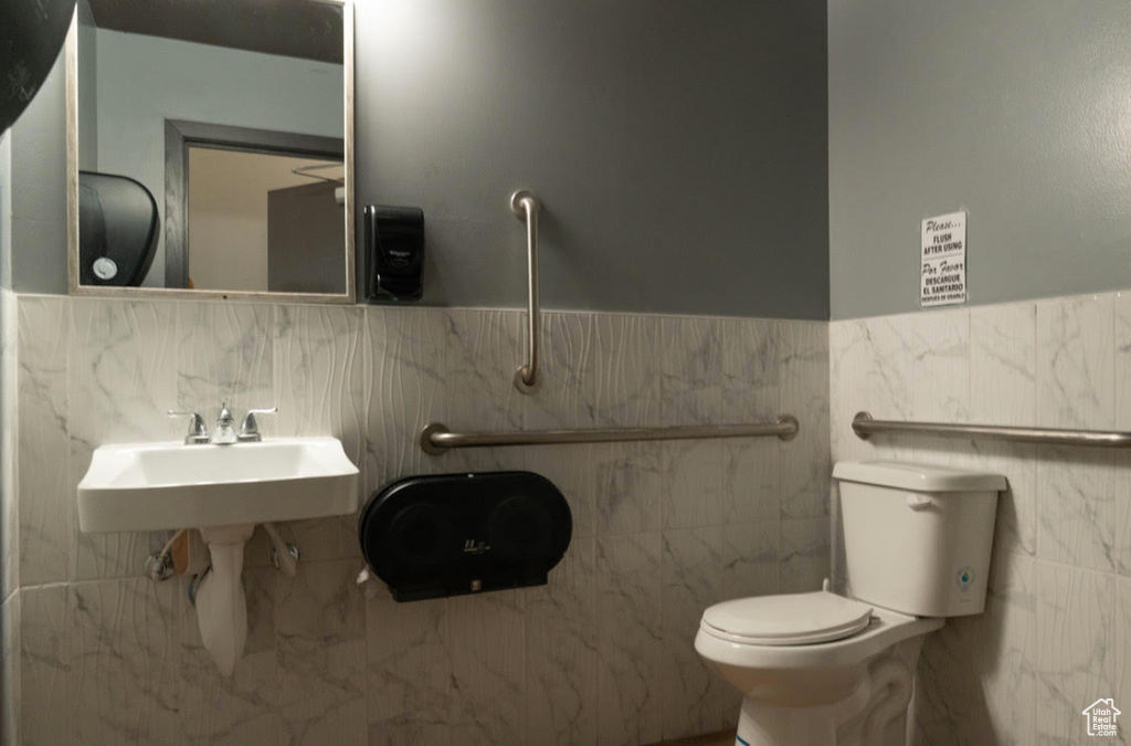 Bathroom featuring tile walls, toilet, and a wainscoted wall